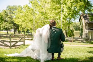 Bride and groom in tender embrace under green trees in outdoor garden.