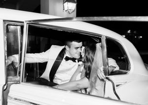 Black and white photo of classic car departure after wedding celebration.