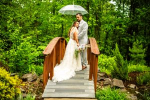 Couple with white umbrella walking along wooden bridge pathway.
