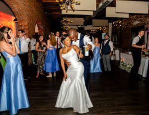 Wedding celebration with guests dancing in a rustic brick-walled venue with blue and white color scheme.