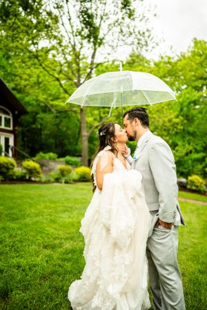 Wedding couple sharing romantic moment under clear umbrella in lush garden setting.