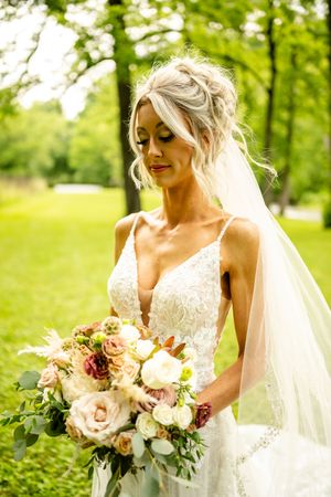 An elegant bridal portrait outdoors featuring a lace gown and blush-toned bouquet.