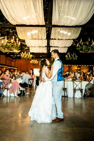 Couple dancing together in an elegant reception hall with white draped ceiling and chandeliers.