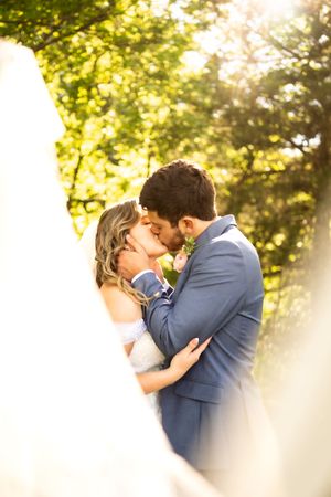 Sunlit wedding portraits through trees showing tender moments between newlyweds.