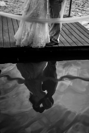 Black and white reflection of a couple on wooden dock over water.