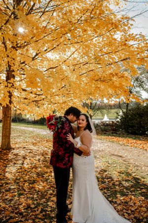 A romantic autumn wedding photoshoot under golden trees with fallen leaves scattered on the ground.