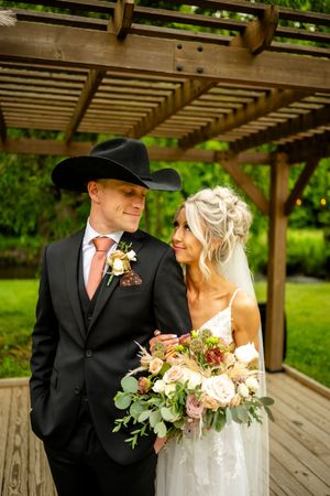 A western-themed wedding portrait under a pergola with cowboy hat and floral bouquet.