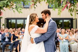 Outdoor wedding ceremony under hanging floral arrangements with guests watching.