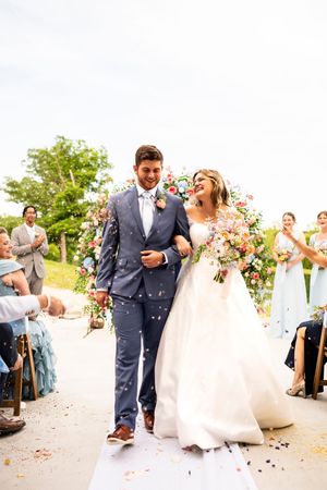 Wedding guests toss flower petals as newlyweds walk down pathway in celebration.