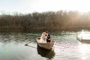 Romantic sunset boat scene on a tranquil lake with trees in the background.