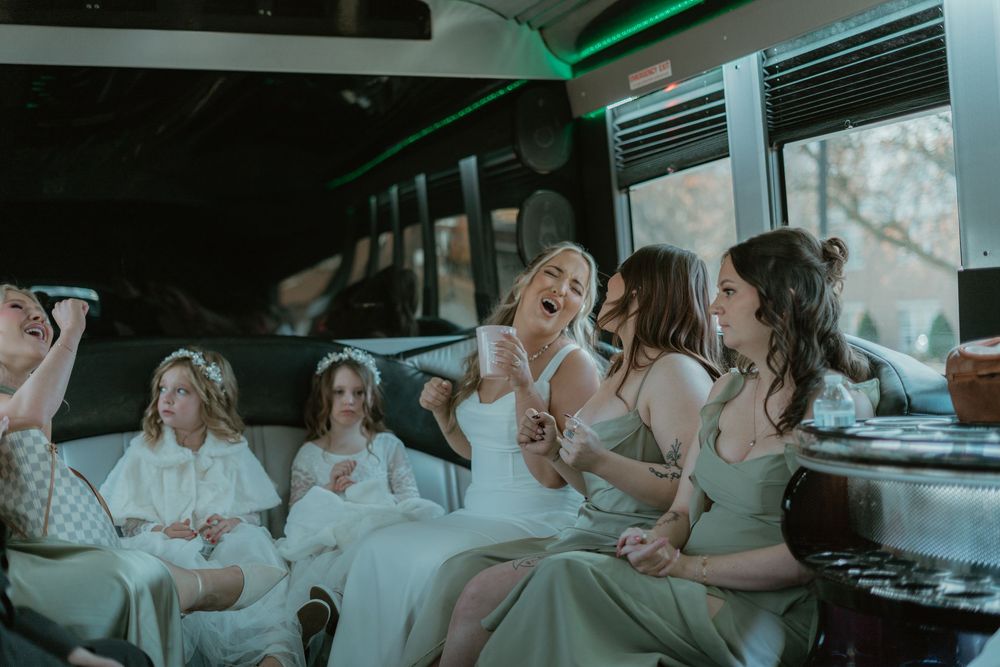 Bride laughing with bridesmaids and flower girls inside a party bus.