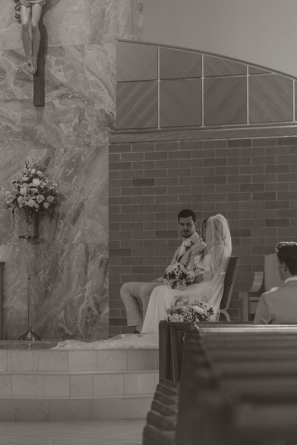 Black and white photo of bride and groom seated at church altar.