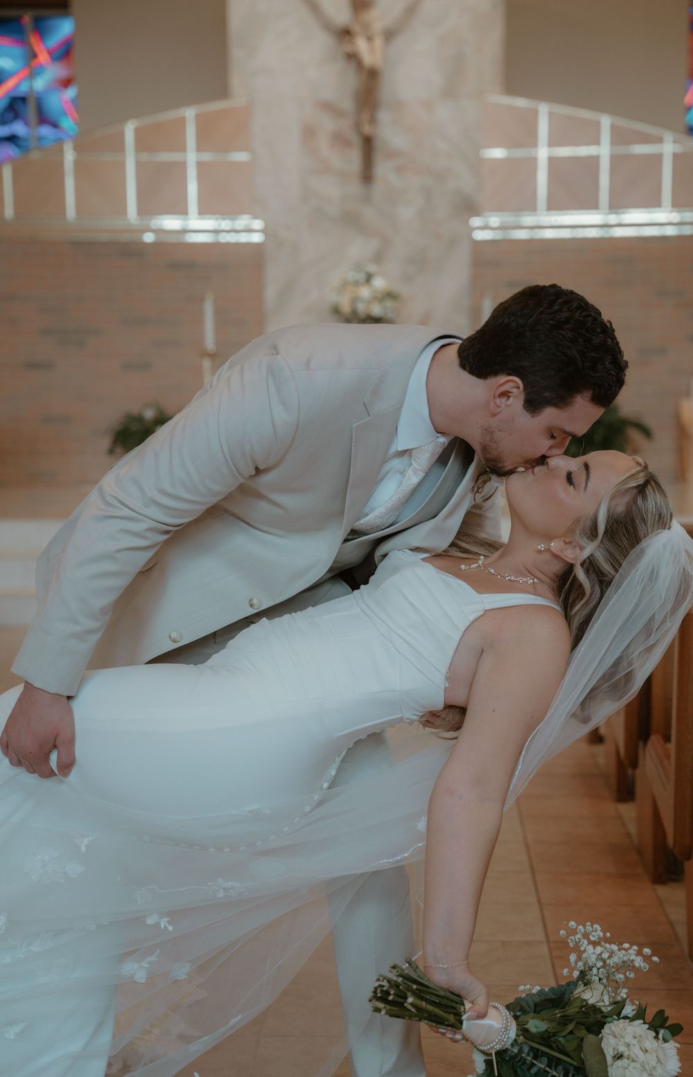 Groom dipping bride for a kiss inside a decorated church after ceremony.