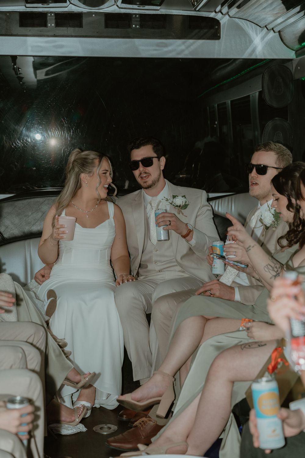Bride and groom sitting together in limo with wedding party holding drinks.