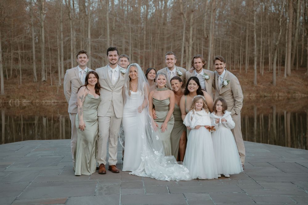 Wedding party posing together in front of a wooded lake backdrop on a fall day.