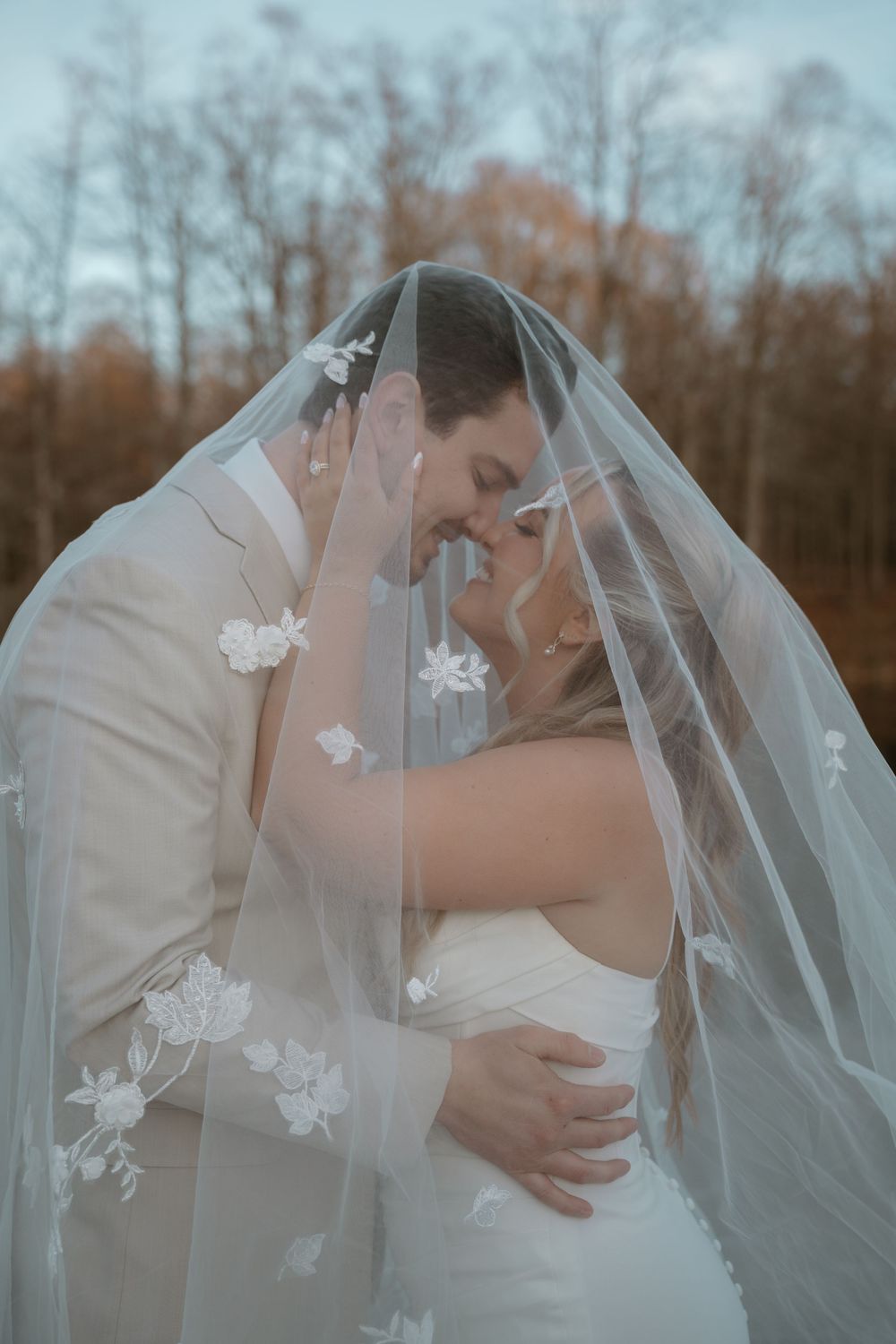 Bride and groom sharing an intimate moment under a floral embroidered wedding veil outdoors.