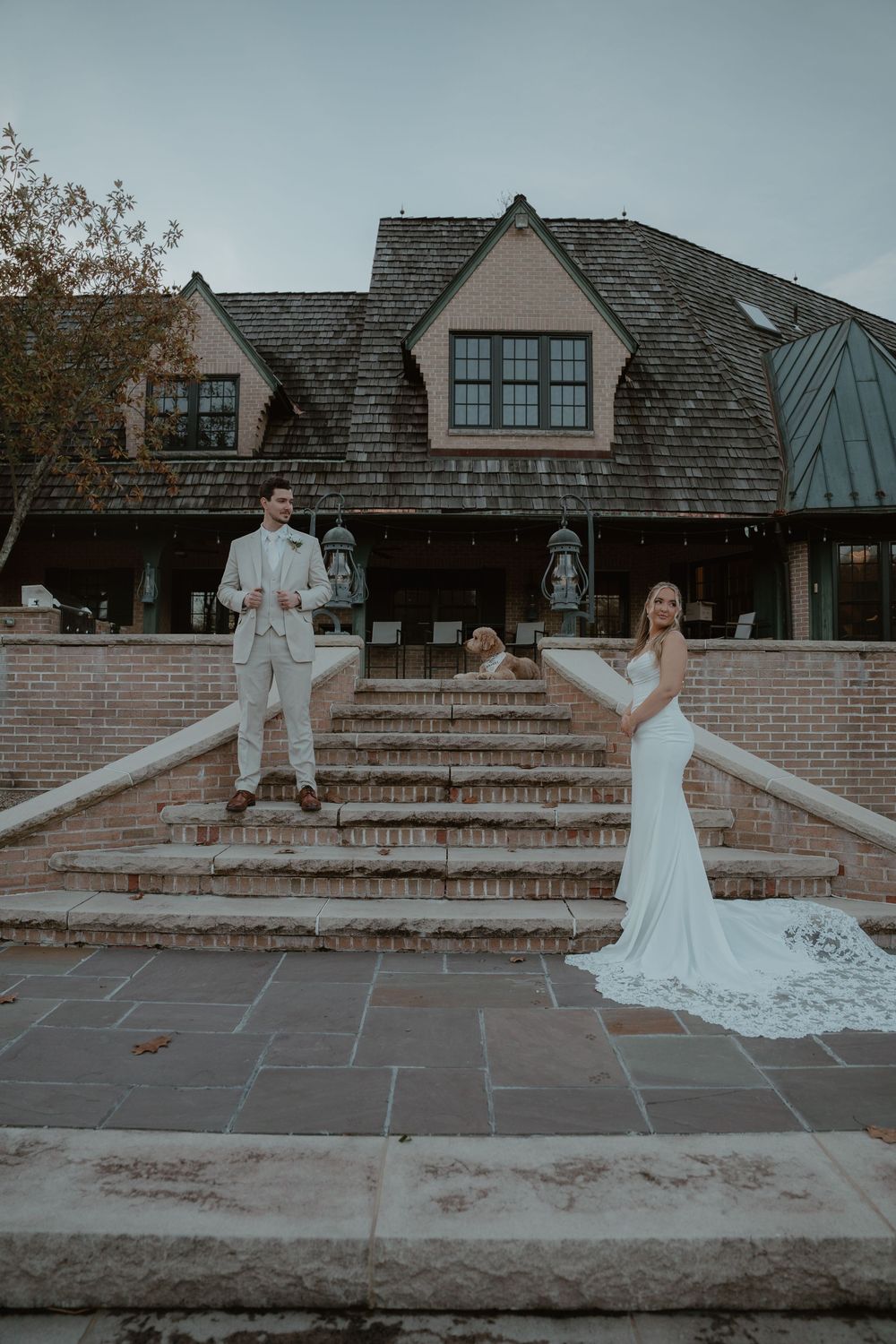 Bride and groom posing on stone steps outside a rustic wedding venue at twilight.