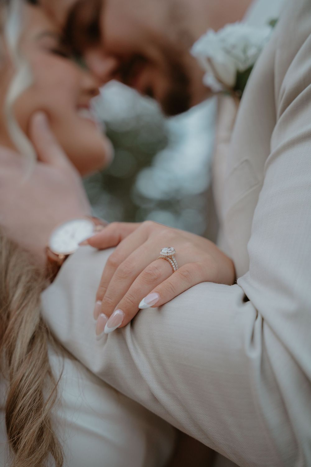 Close-up of bride's diamond engagement ring as she embraces the groom in a beige suit.
