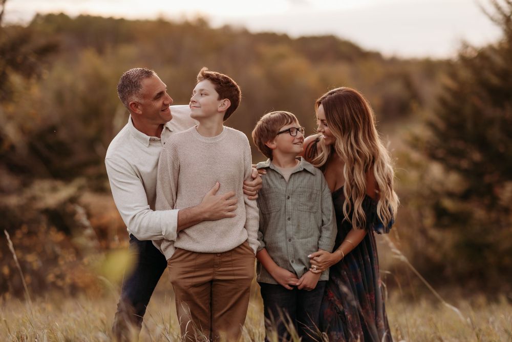 Family of four posing outdoors in a golden field during autumn, sharing a warm and joyful moment together.