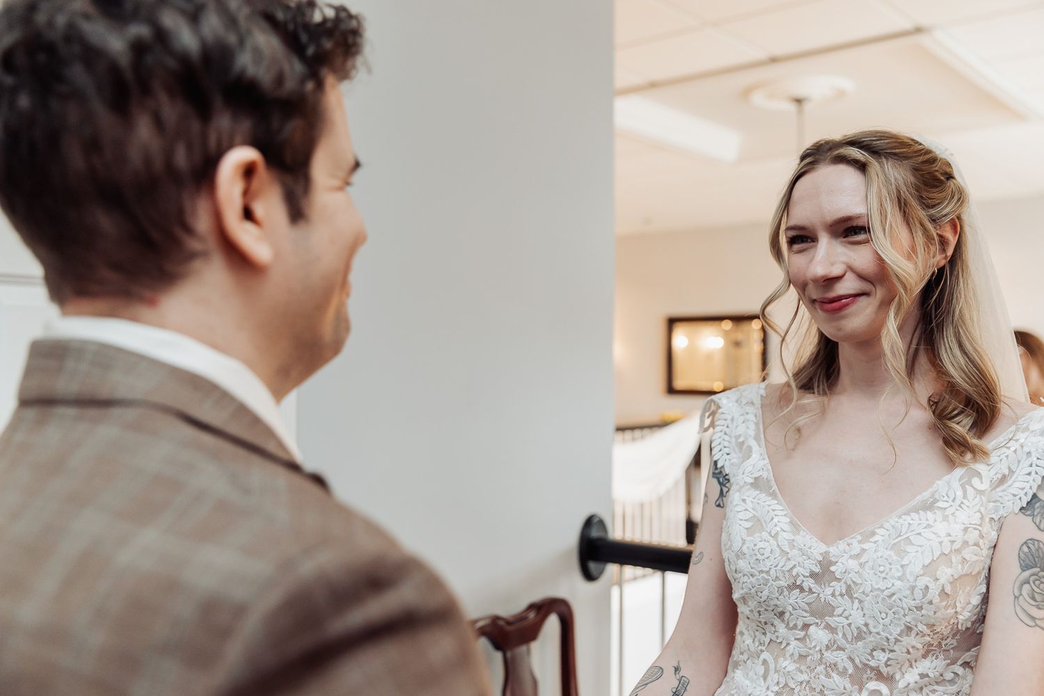 Bride in lace gown smiles at groom in plaid suit during an intimate wedding first look moment.