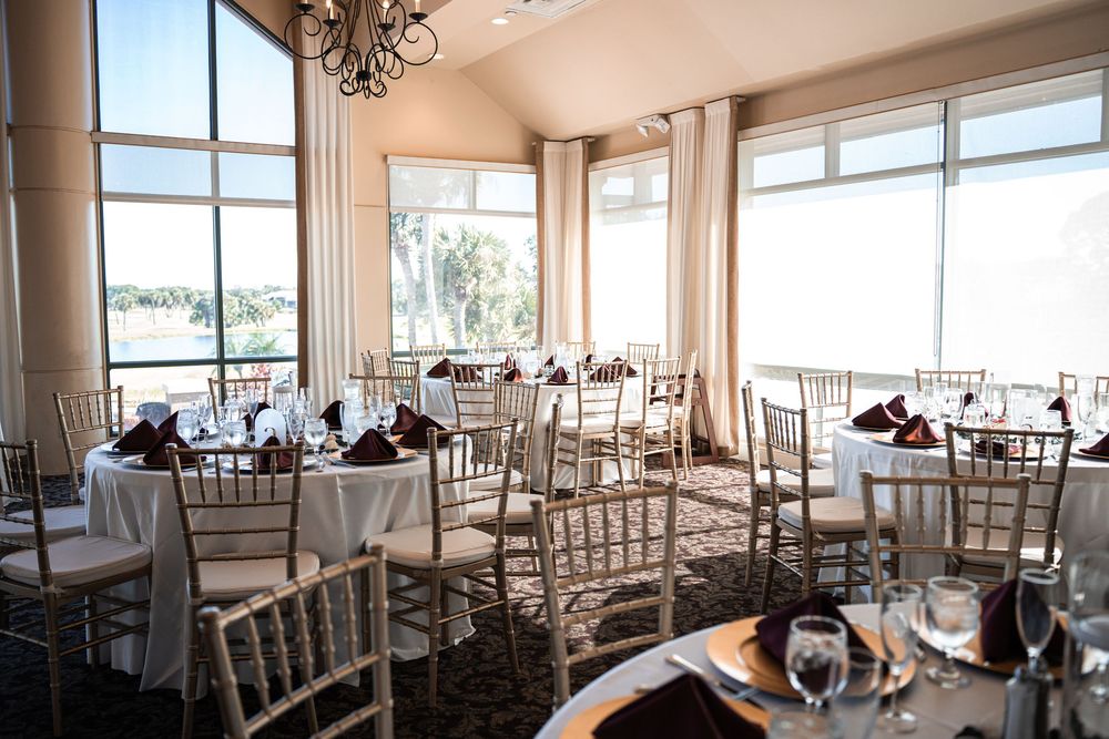 Elegant banquet hall with chiavari chairs, white-draped tables, and large windows overlooking a waterfront view.