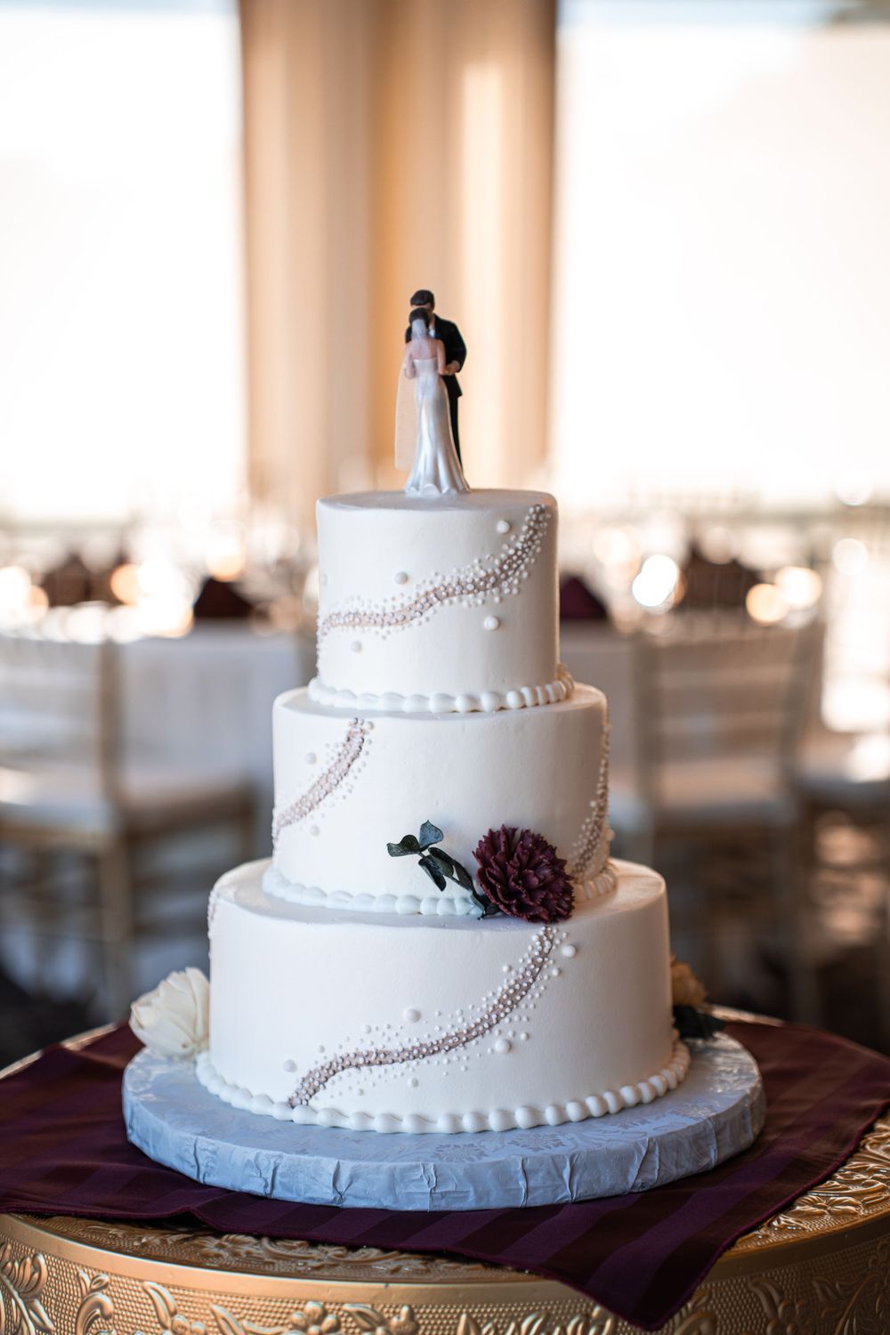 Elegant three-tier white wedding cake with pearl details, floral accents, and bride and groom cake topper.