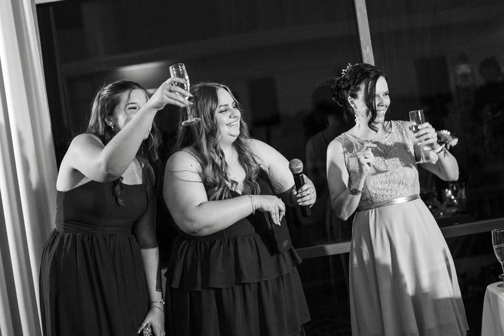 Bridesmaids raising glasses in a toast during a wedding reception in black and white photo.