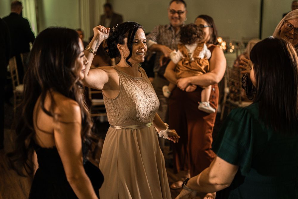Bride in beaded gown dancing joyfully with guests at a lively wedding reception celebration.