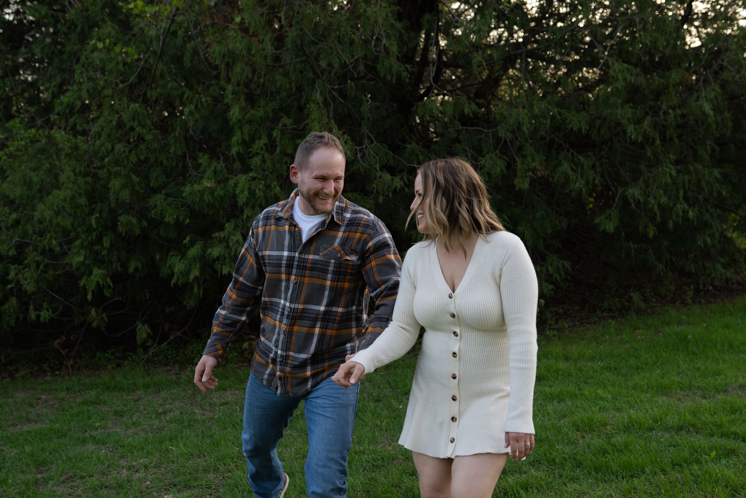 Couple holding hands and walking together outdoors on green grass with trees in background.