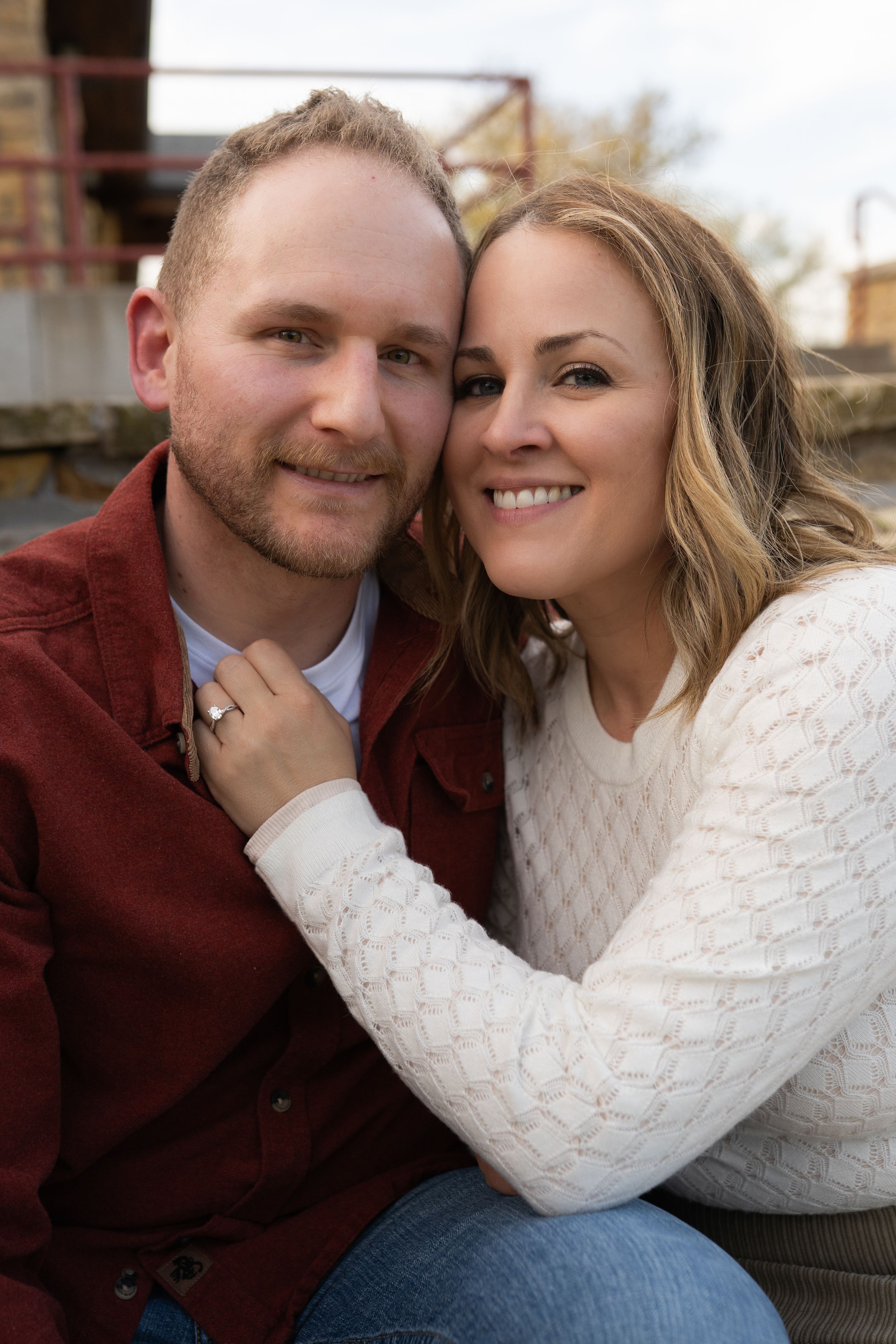 Smiling couple in casual attire posing cheek to cheek outdoors in a warm engagement photo.