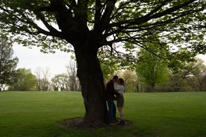 Romantic couple embracing under a large tree in a lush green park during spring.