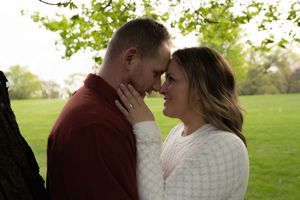 Romantic couple touching foreheads near a tree in a green park setting.