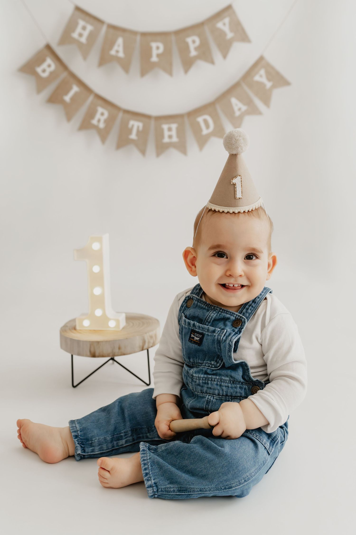 Geburstagsfotoshooting zum ersten Geburtstag im Fotostudio Stockerau, Bub lächelt fröhlich mit Partyhut und Girlande