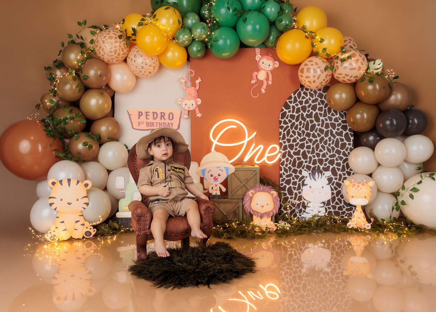 Safari-themed first birthday party setup with balloon arch, jungle animals, and neon “One” sign for baby Pedro.