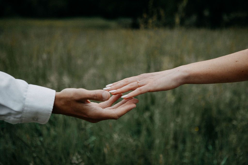 Two hands gently reaching toward each other in a romantic outdoor setting with lush green grass background.