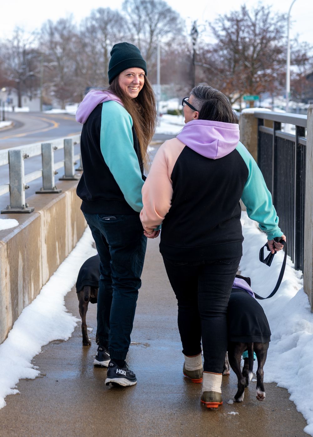 Female/female couple walking dogs on snow covered bridge