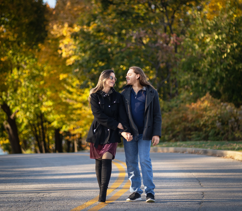 Couple holding hands walking on a road surrounded by colorful autumn trees during fall season.