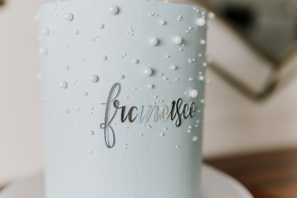 Light blue cake decorated with white pearl dots and elegant silver script reading franasee.