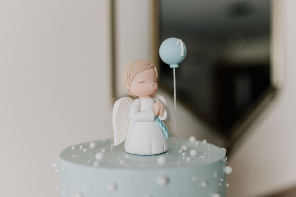 A delicate angel figurine holding a blue balloon atop a light blue cake decorated with pearl details.