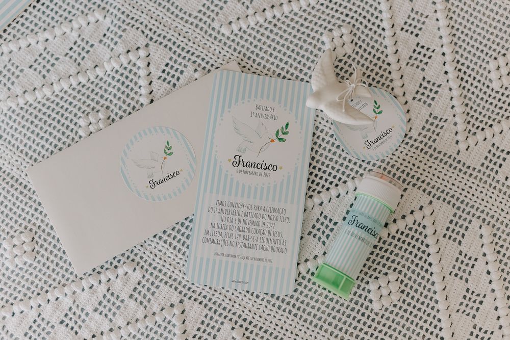 Elegant baptism invitation set with blue stripe card, envelope, and personalized lip balm favor on lace tablecloth.