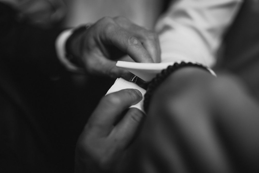 Close-up black and white photo of hands fastening a cufflink on a wedding shirt sleeve.