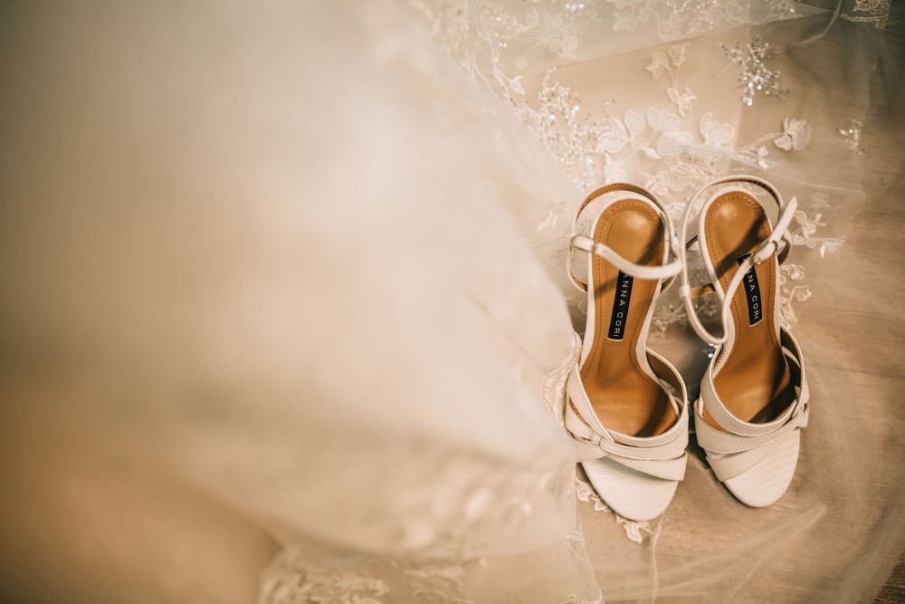Elegant strappy ivory bridal heels resting on lace wedding dress fabric for wedding day.