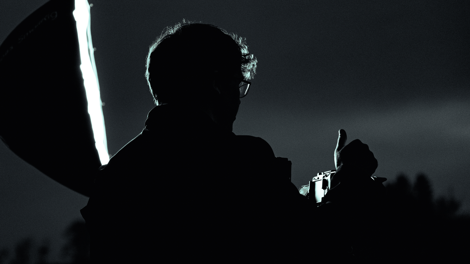 Two filmmakers operating professional cameras on a film set inside a warmly lit room.