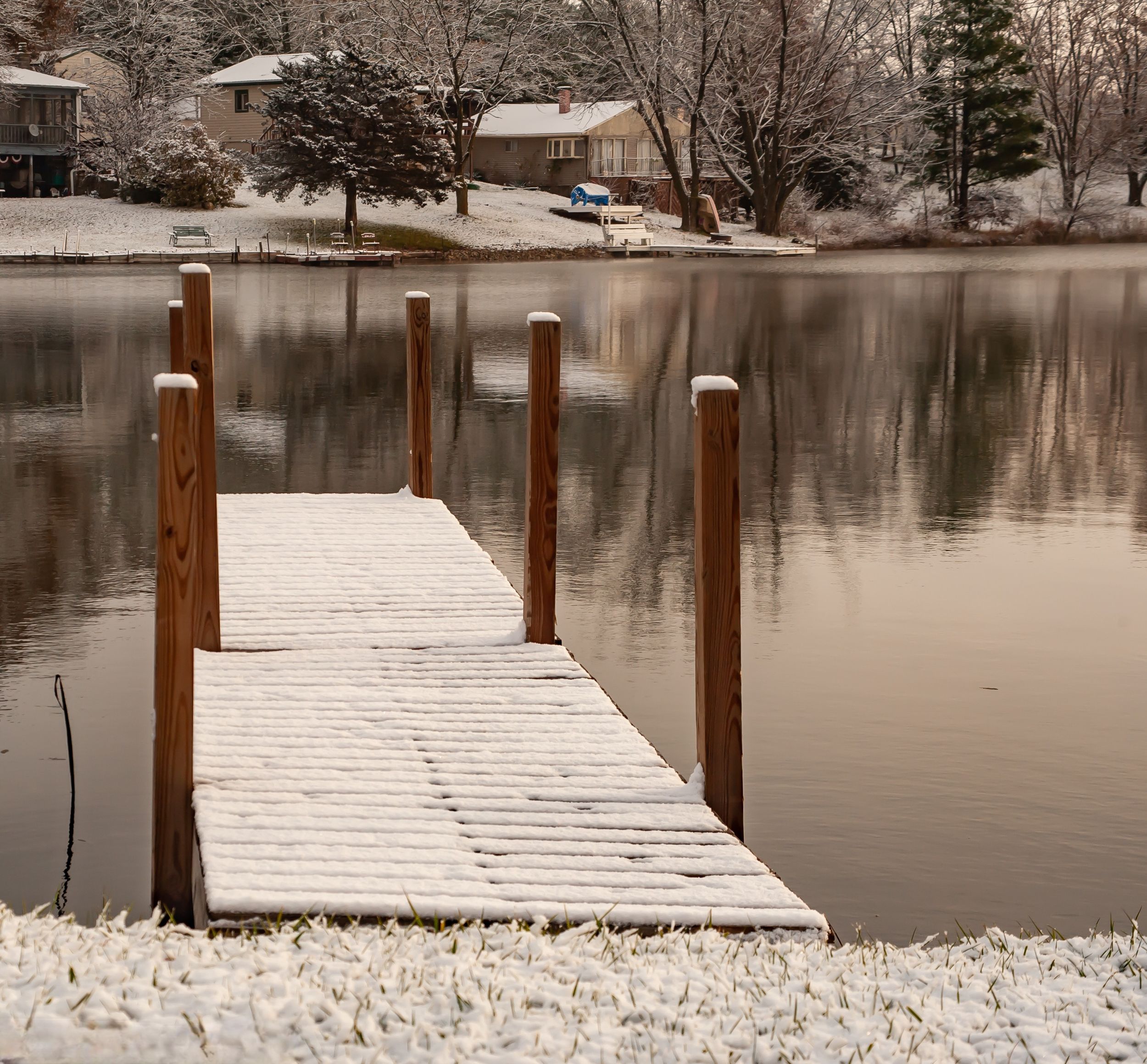 Snow covered wooden dock on still lake in winter Northern Missouri with lake houses reflecting in water