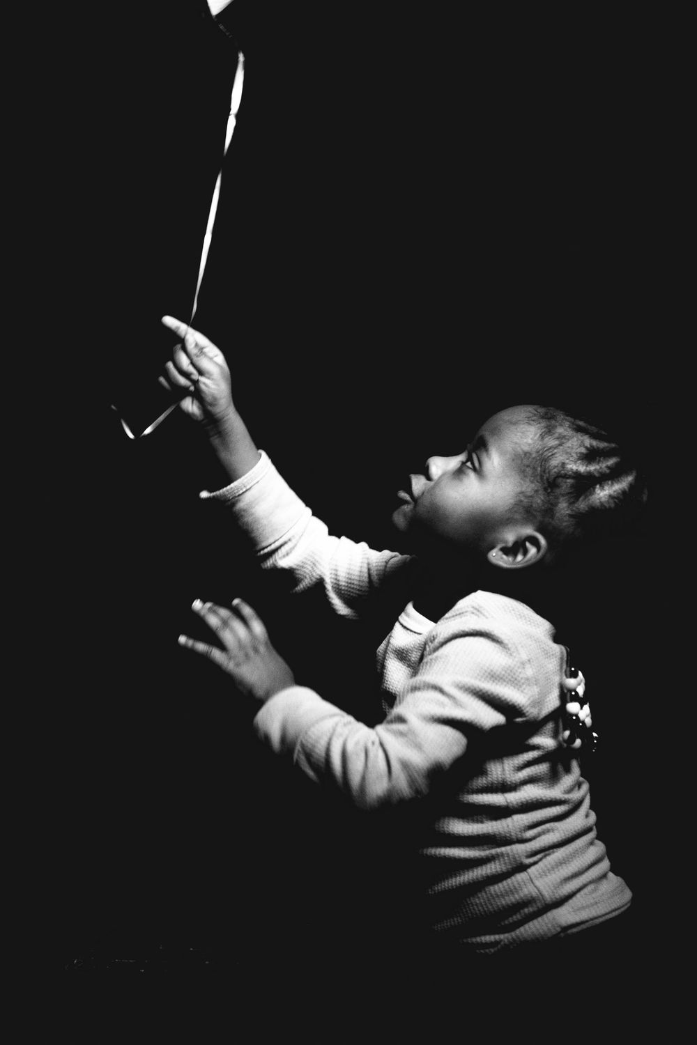Black and white photo of a young child reaching up toward a balloon in the dark.