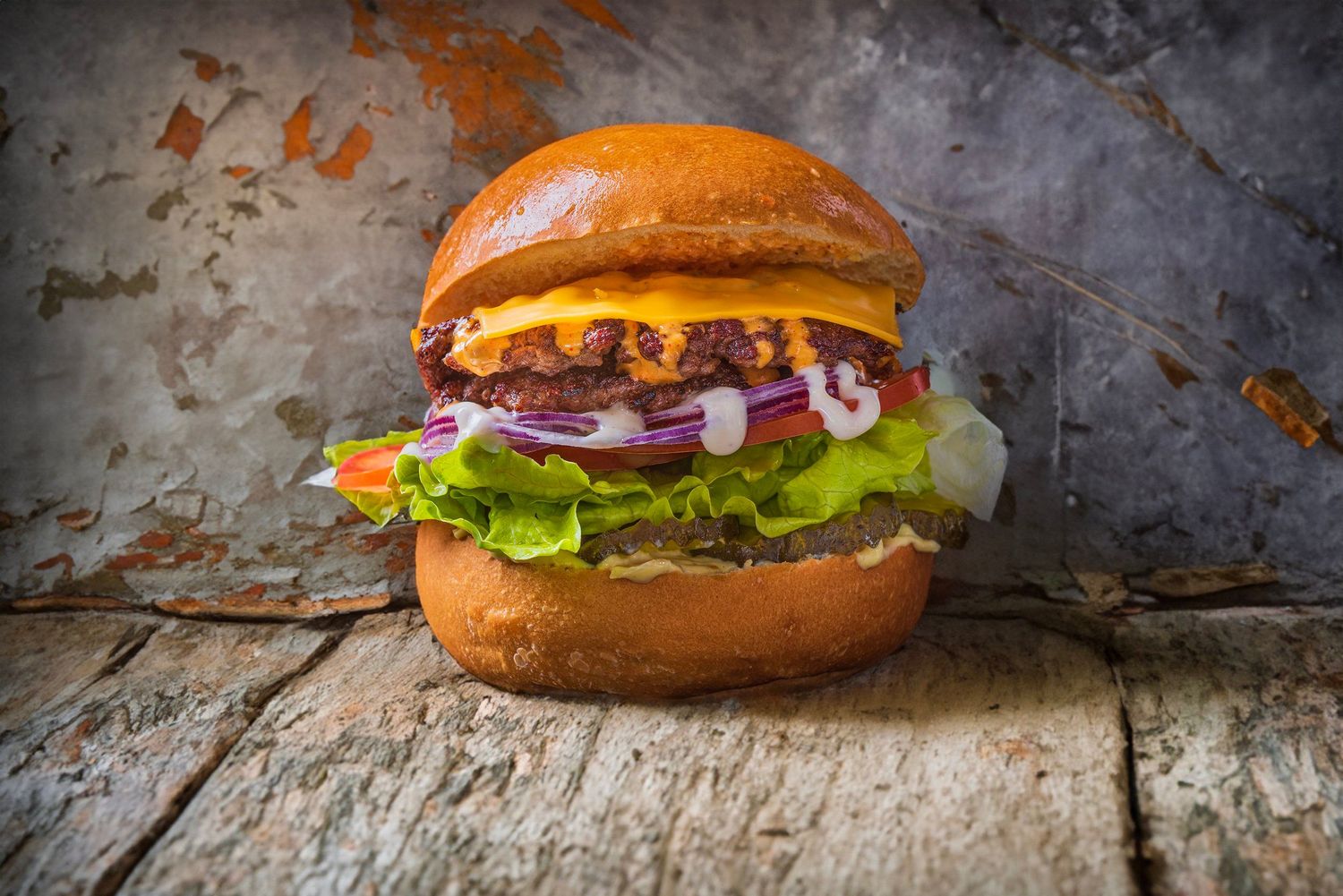 A gourmet burger with beef patty, lettuce, onions, and cheese on a toasted bun, photographed on rustic wooden surface.