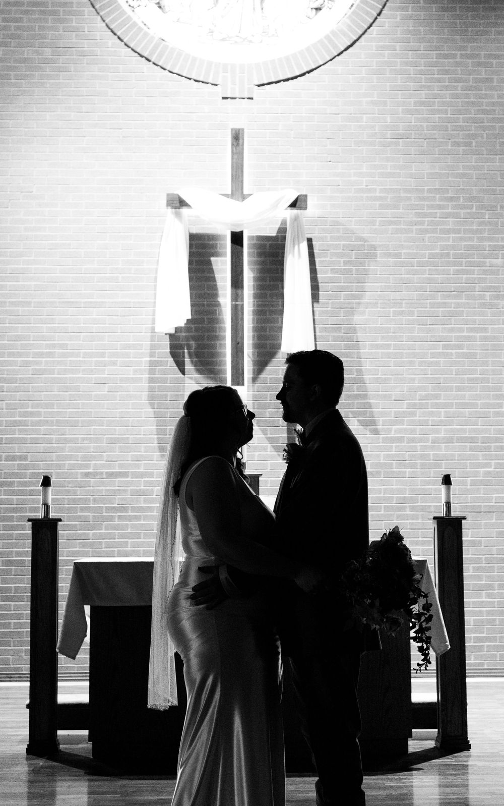 Black and white silhouette of bride and groom facing each other at church altar during wedding ceremony.