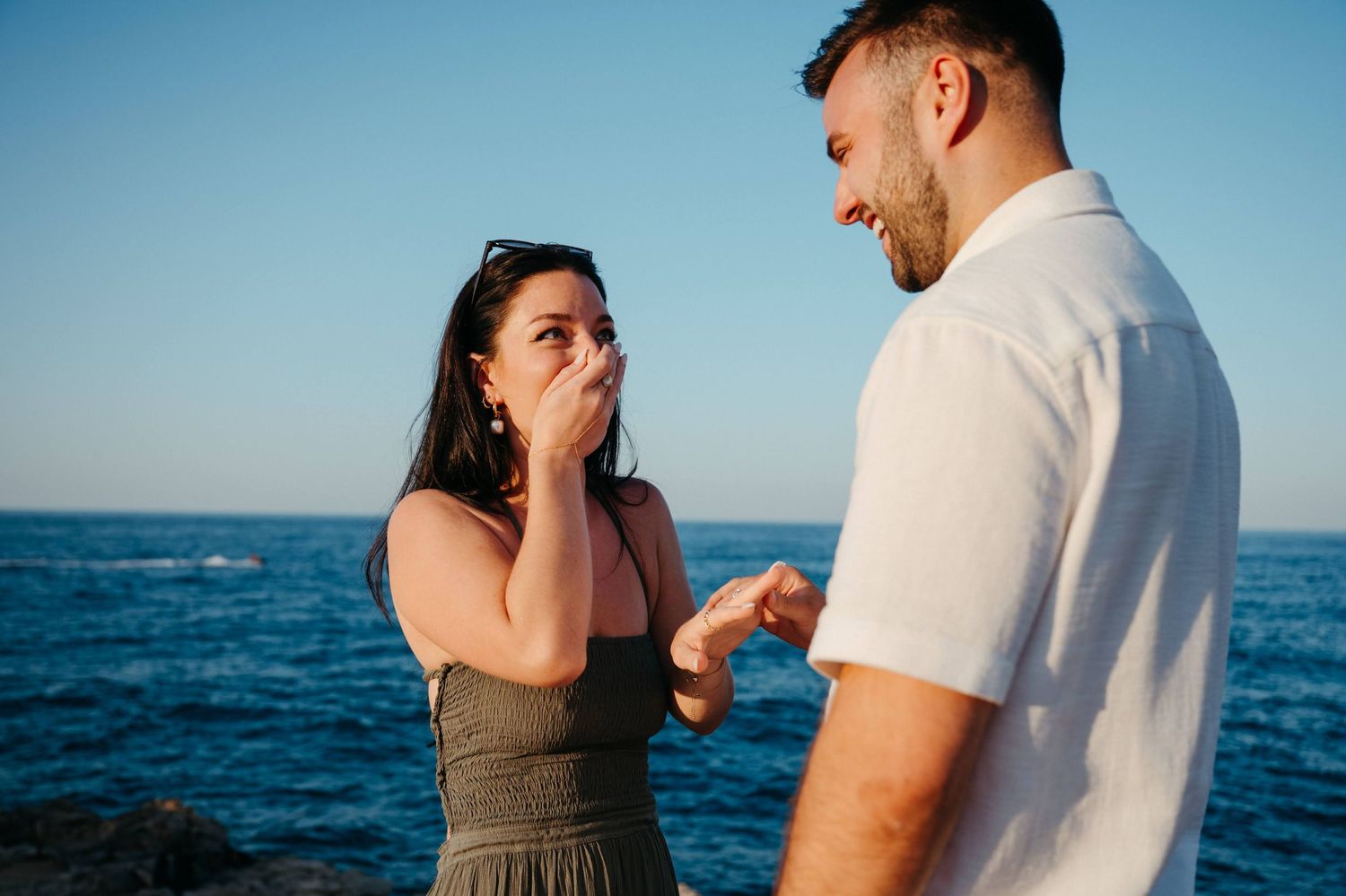 Two hands reaching toward each other with rings and watches, framed by a stone arch with ocean view.