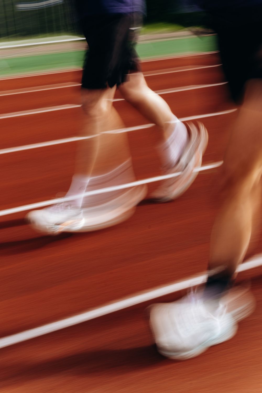 Blurred motion shot of runners in white sneakers racing on a red athletic track with white lane lines.