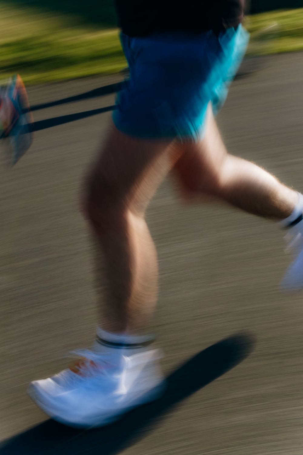 Close-up motion blur of a runner's legs in blue shorts and white sneakers on a paved road.